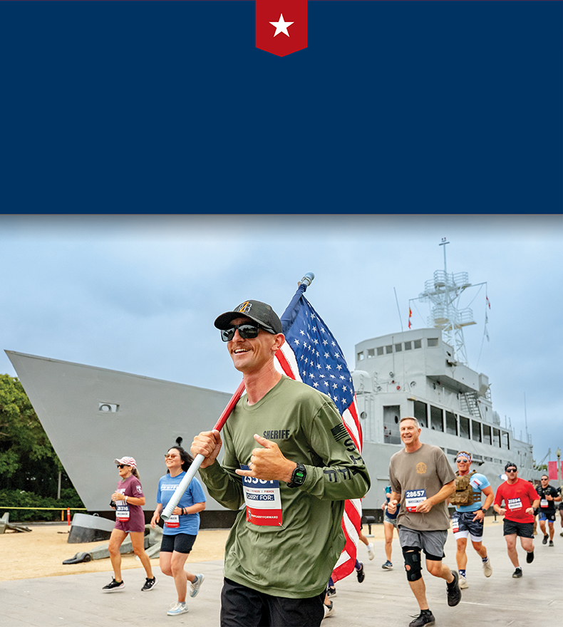 A WWP supporter in a green shirt holds an American flag over his shoulder while running in a Carry Forward 5K race.