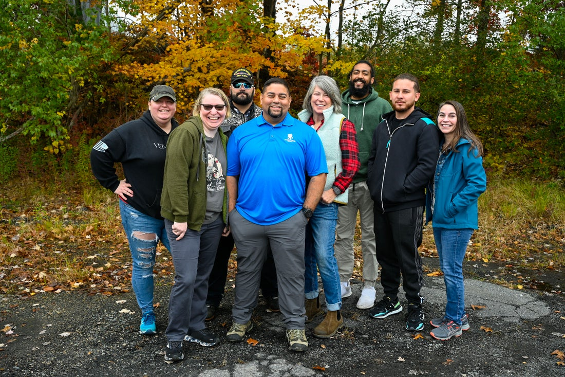 A group of warriors stand smiling as a group while standing outside on a fall day.
