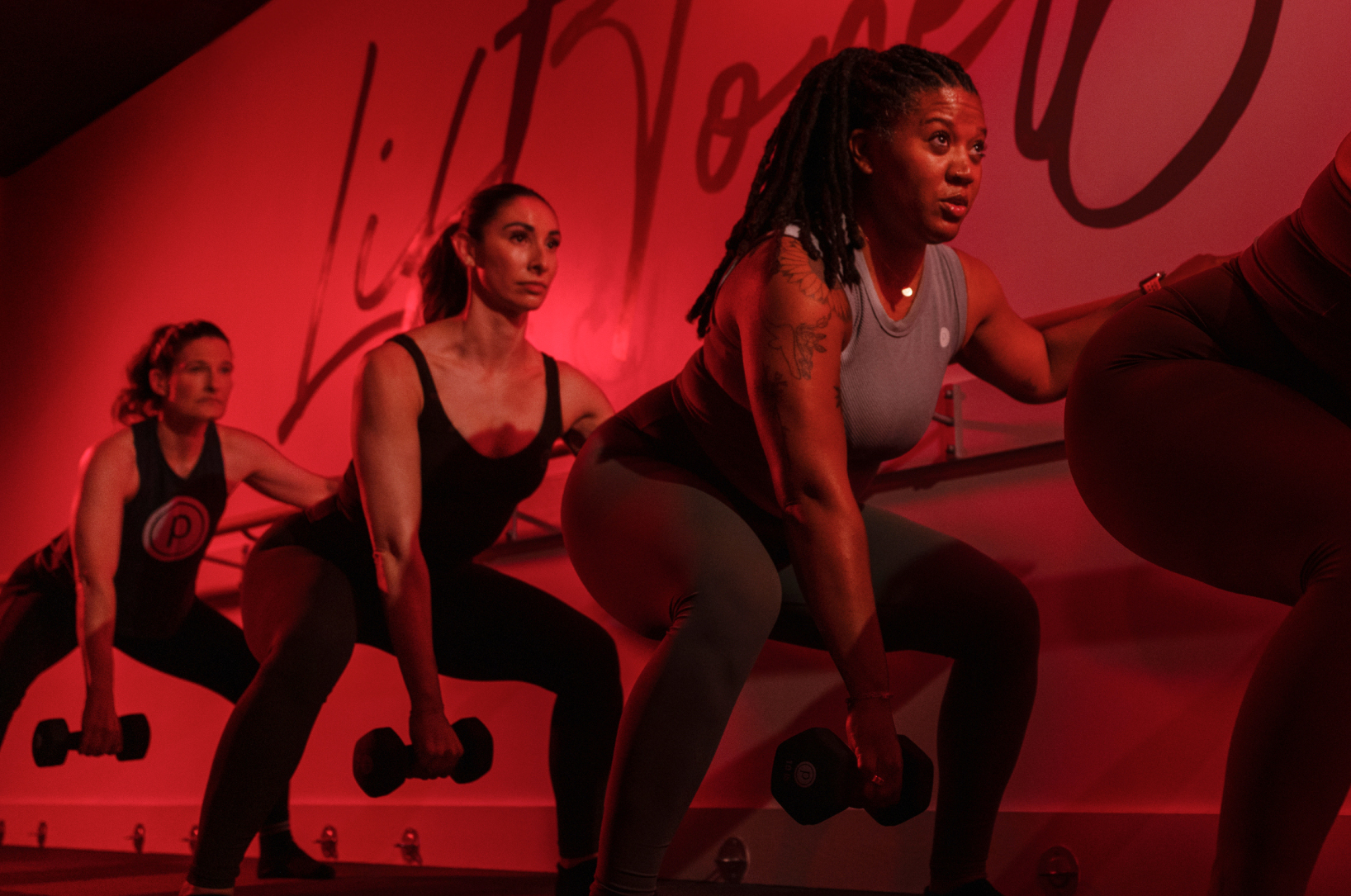 Members taking a define class, squatting a heavier dumbell at the barre
